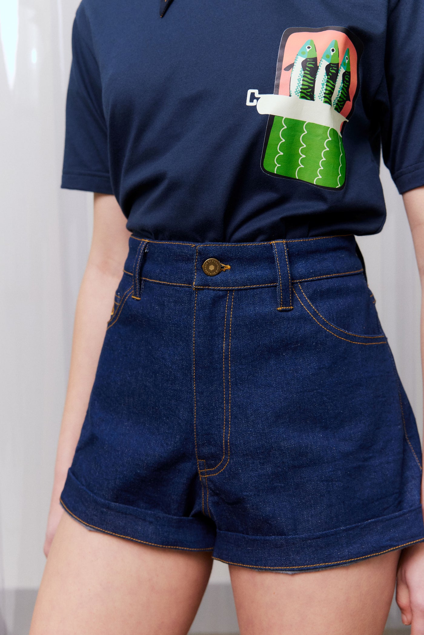 Person wearing a navy blue t-shirt with a colorful pocket design and dark blue denim shorts.