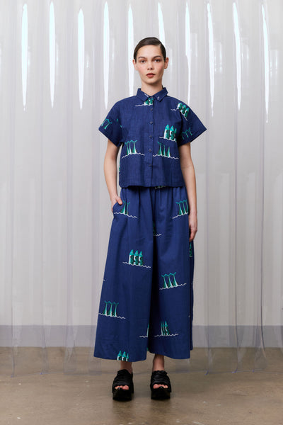 Person wearing a blue outfit with green patterns against a white curtain background