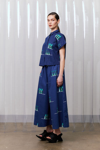 Woman wearing a blue outfit with green patterns against a white curtain background