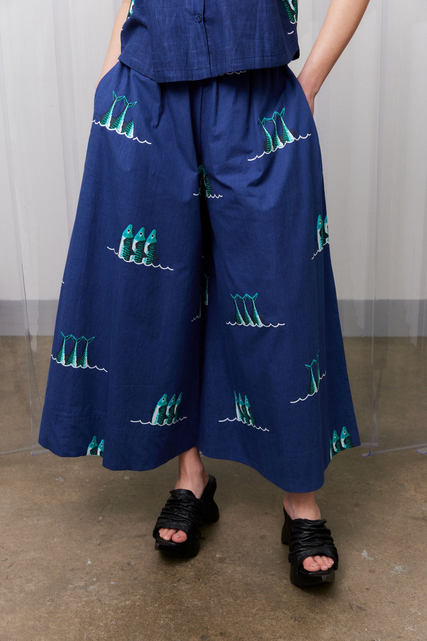 Navy blue pants with green patterns worn by a person on a plain background