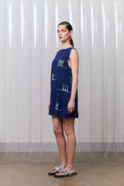Woman wearing a navy blue dress with green patterns against a white curtain background
