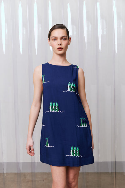 Woman wearing a navy blue dress with green and white patterns against a light curtain background
