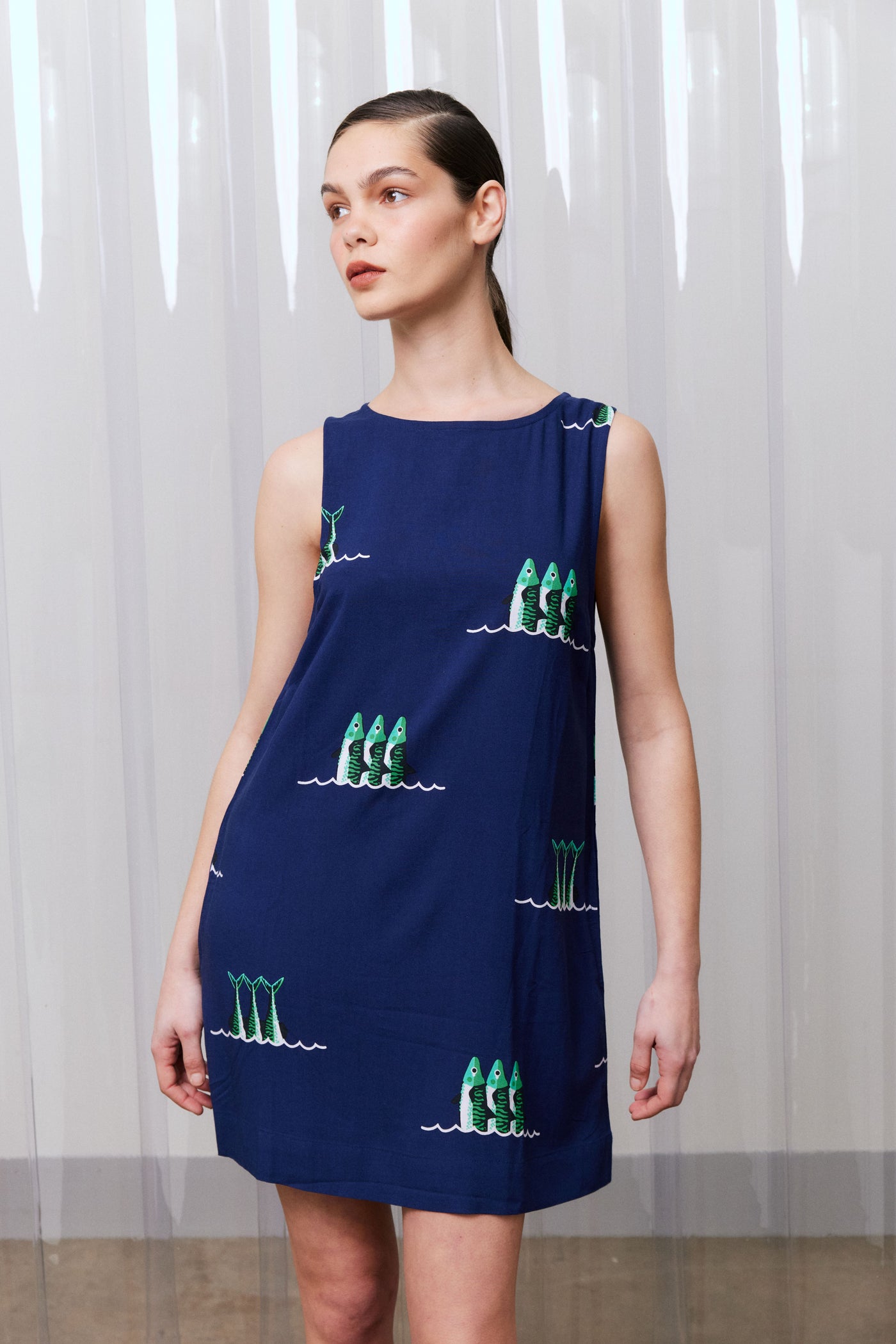 Woman wearing a navy dress with green sardine patterns against a white curtain background