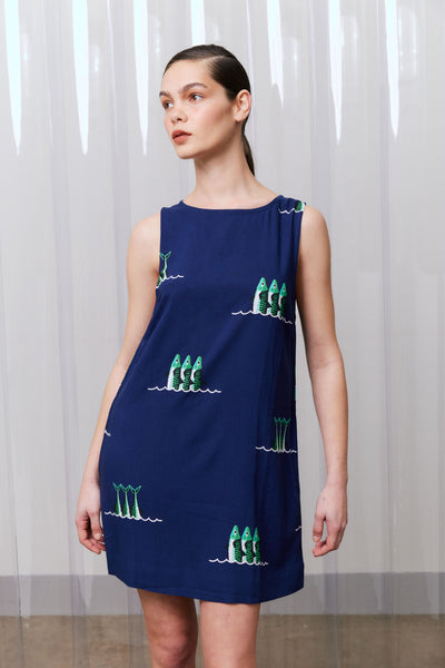 Woman wearing a navy dress with green sardine patterns against a white curtain background