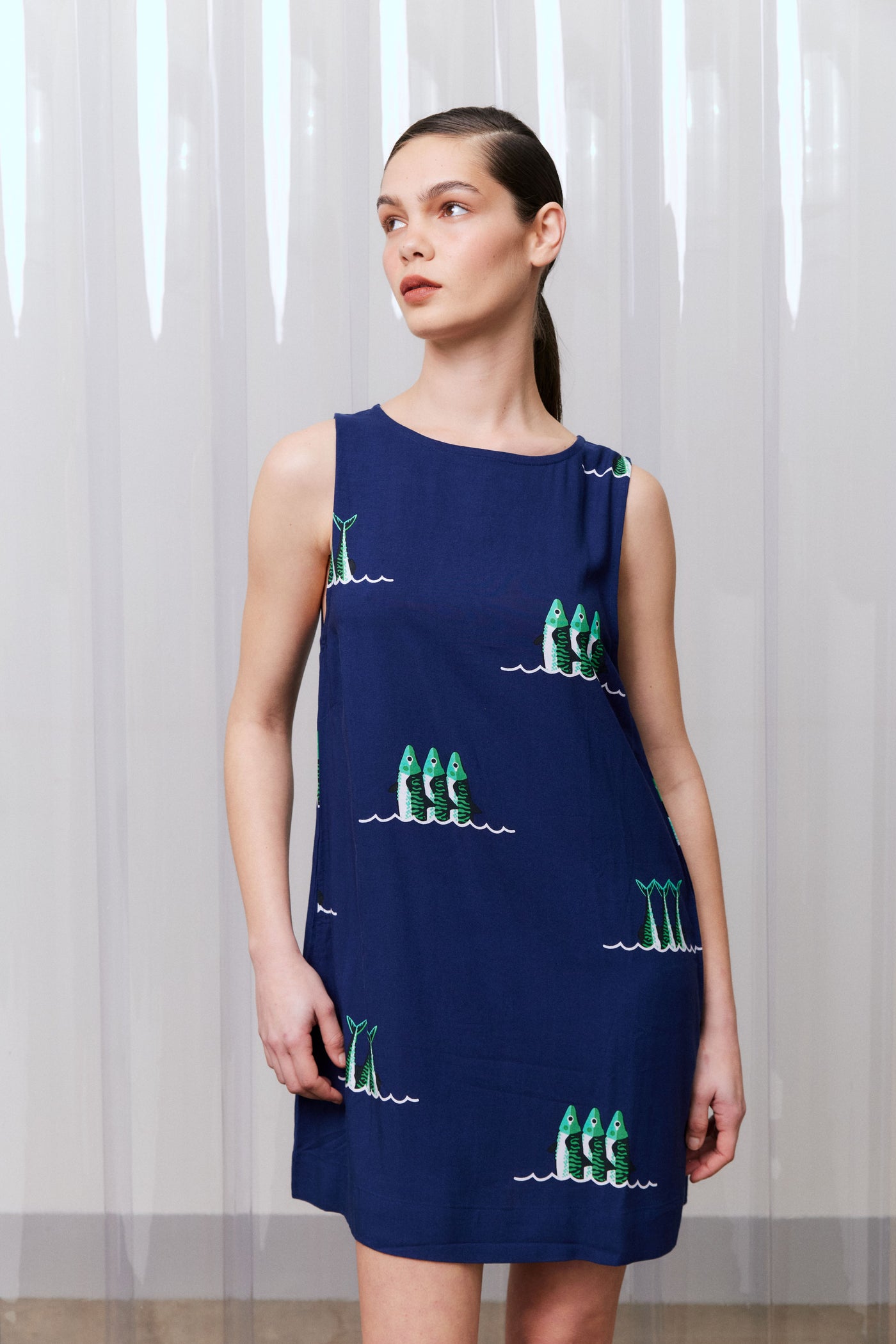 Woman wearing a navy dress with green sardine patterns against a white curtain background