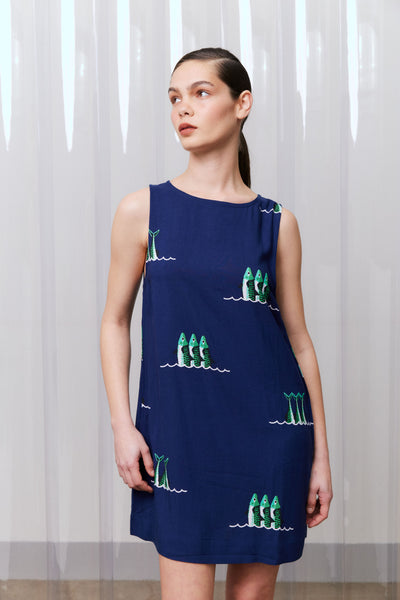 Woman wearing a navy dress with green sardine patterns against a white curtain background