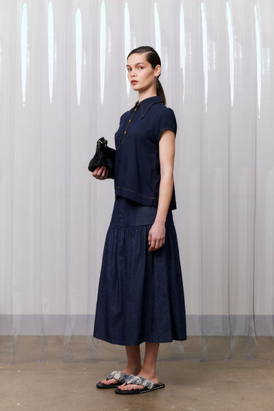 Woman wearing a navy blue outfit against a white curtain background