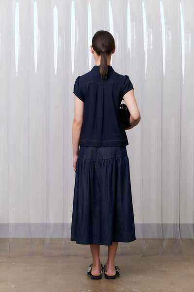 Person wearing a navy blue outfit standing against a white curtain.