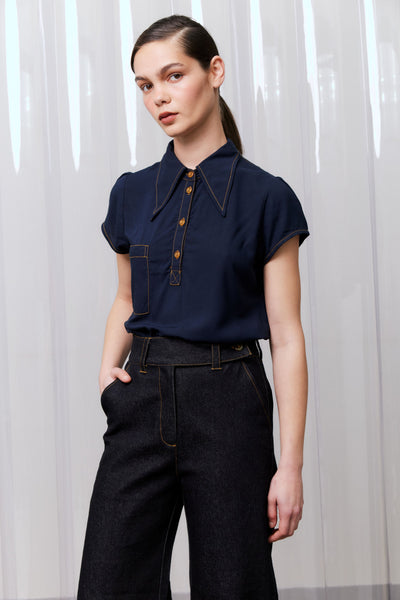 Woman wearing a navy blue shirt with brown buttons against a white curtain background