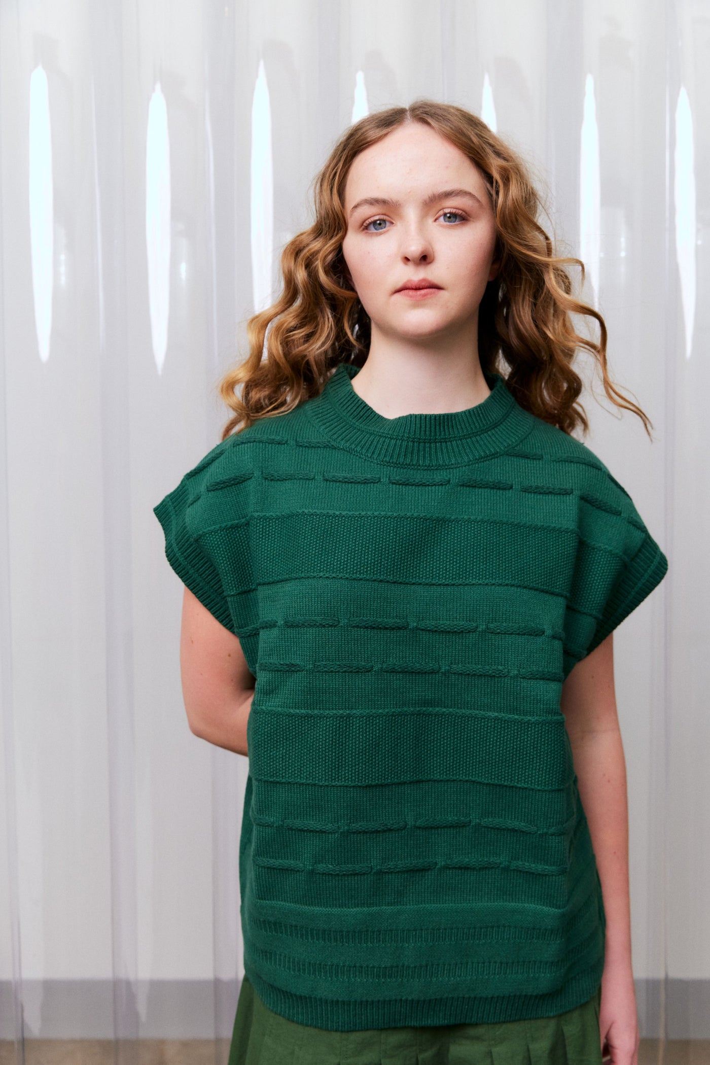 Woman wearing a green textured top against a white curtain background