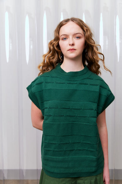 Woman wearing a green textured top against a white curtain background