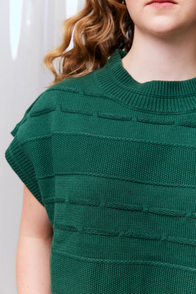 Green knitted top worn by a person with a blurred background