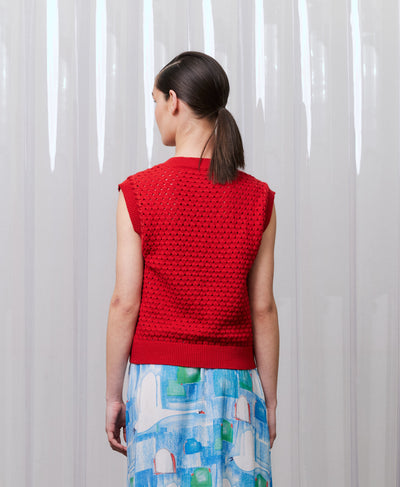 Person wearing a red sleeveless crochet top with a patterned skirt against a white curtain background
