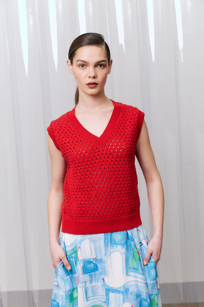 Woman wearing a red sleeveless top with a patterned skirt against a white curtain background