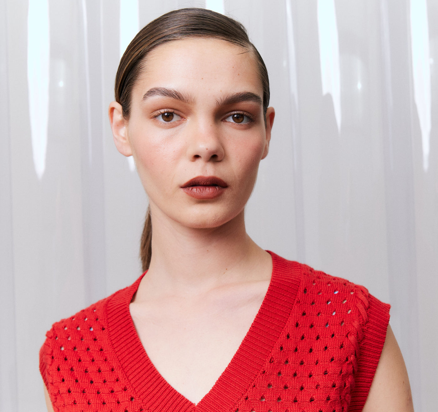 Woman wearing a red sleeveless knitted top against a white curtain background