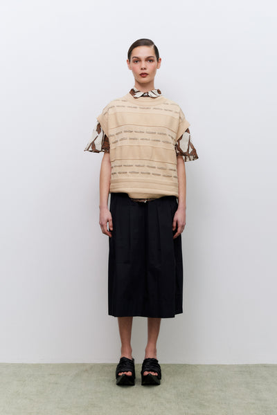 Model wearing a beige top with black trim and a black skirt against a white background