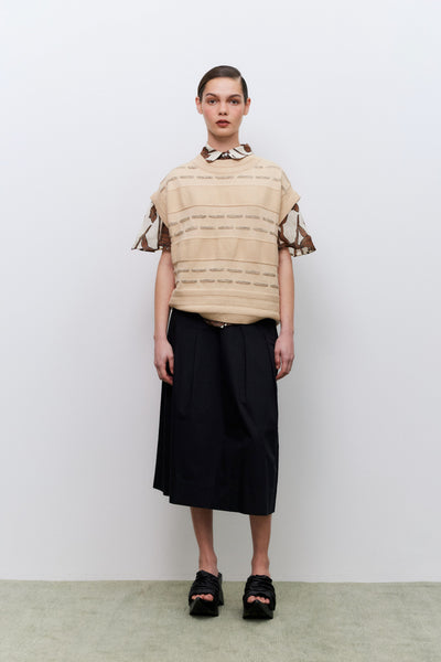 Person wearing a beige striped vest over a patterned shirt and black skirt against a white background