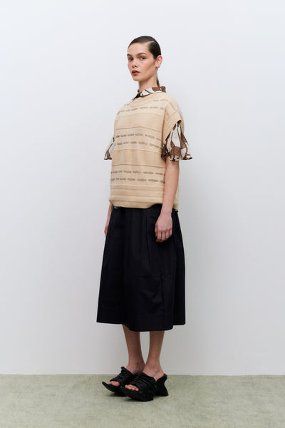 Woman wearing a beige top with brown details and a black skirt on a white background