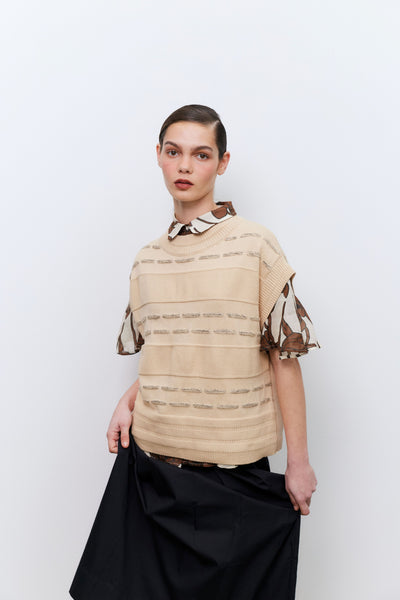 Model wearing a beige vest over a patterned top with black skirt against a white background