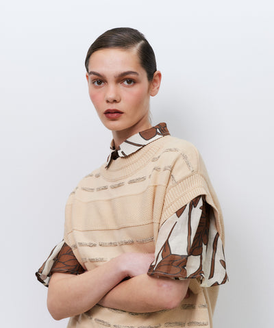 Model wearing a beige vest over a patterned top against a white background