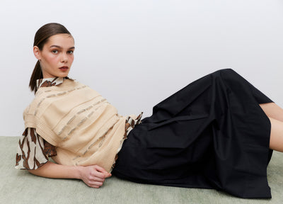 Woman lying on a light-colored surface wearing a beige top and black skirt.