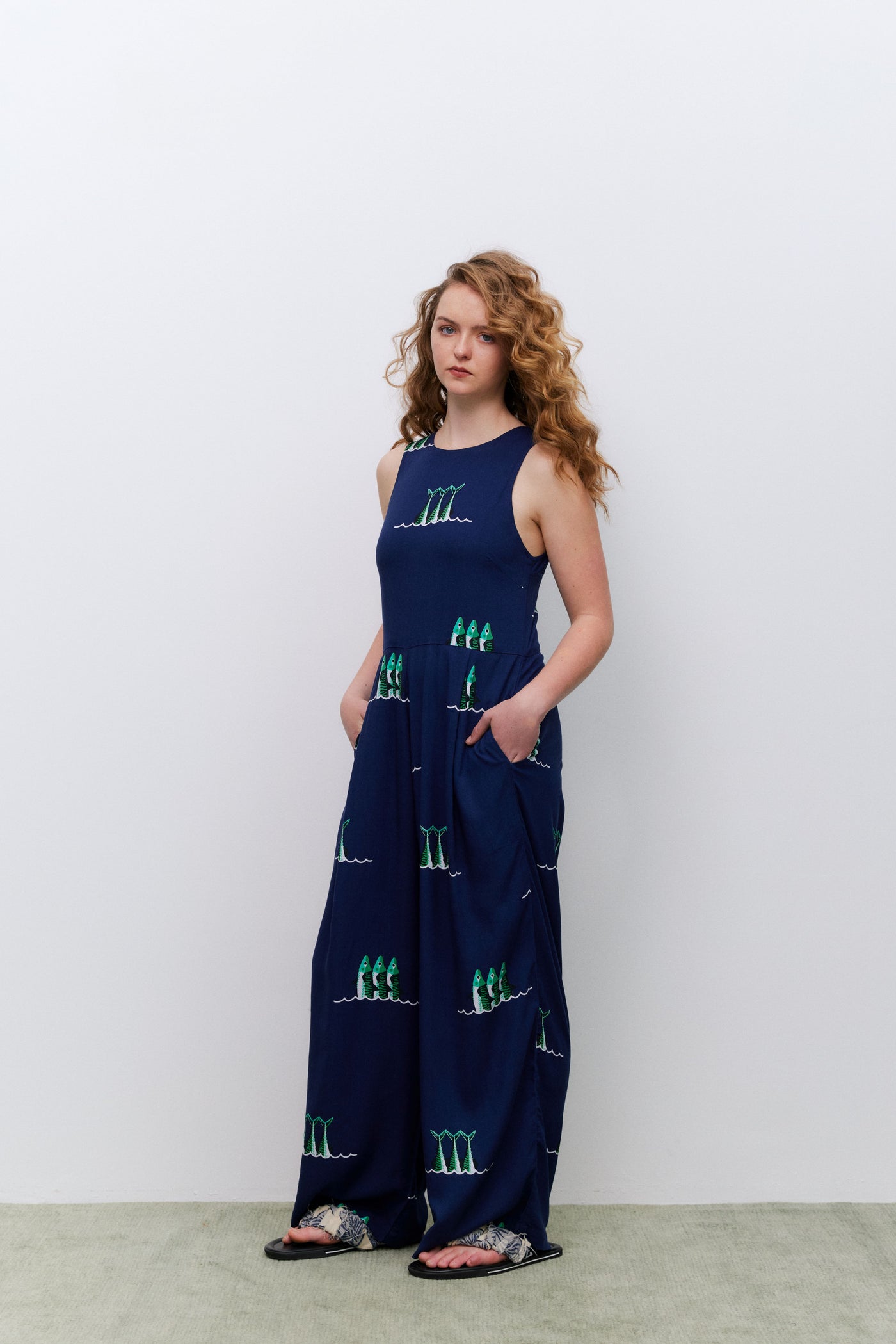 Woman wearing a navy blue sleeveless jumpsuit with green patterns against a white background