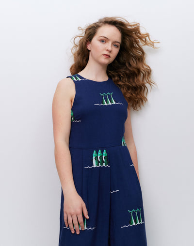 Woman wearing a navy jumpsuit with green sardine print against a white background
