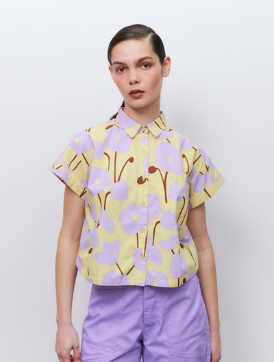 Model wearing a floral blouse and purple pants against a plain background