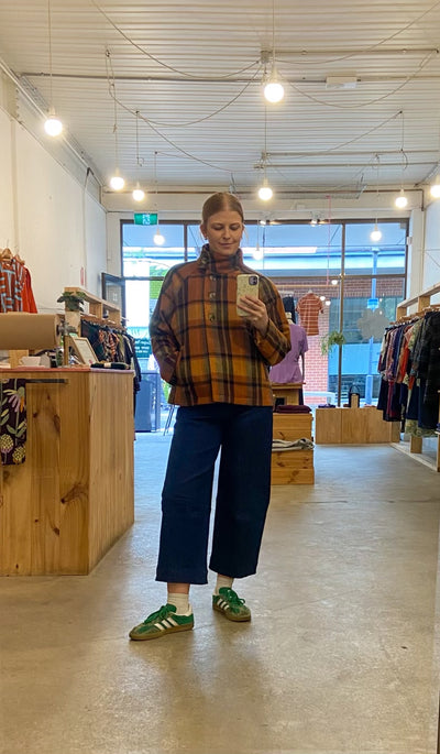 Person taking a mirror selfie in a store wearing a plaid jacket and blue jeans.
