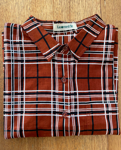 Plaid shirt with orange, black, and white pattern folded on a wooden surface