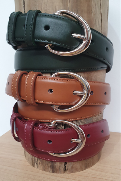 A stack of three leather belts in Tan, Dark Green, and Cherry Red colors, each featuring a top-stitched design and a silver oval belt buckle.