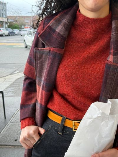 Person wearing a red sweater and plaid coat on a city street