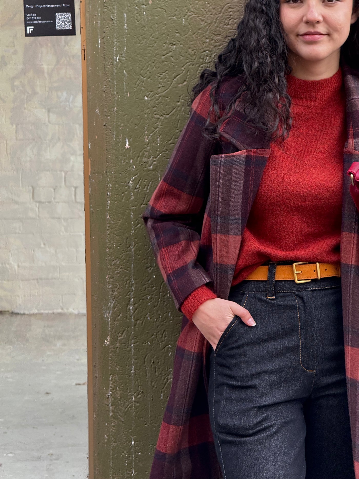 Person wearing a red sweater and plaid coat against a green wall.