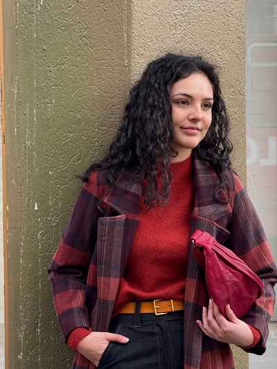 Woman wearing a red sweater and plaid jacket against a textured wall.