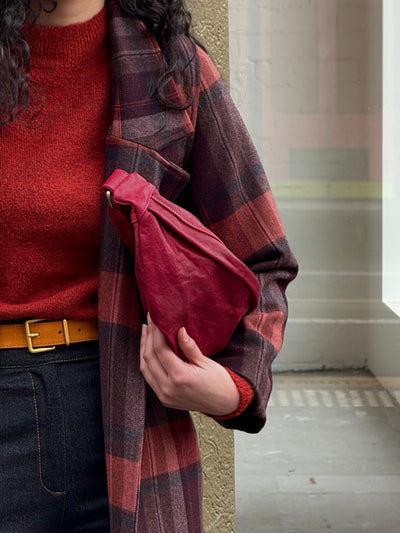 Person wearing a red sweater, plaid coat, and holding a red bag in an urban setting.