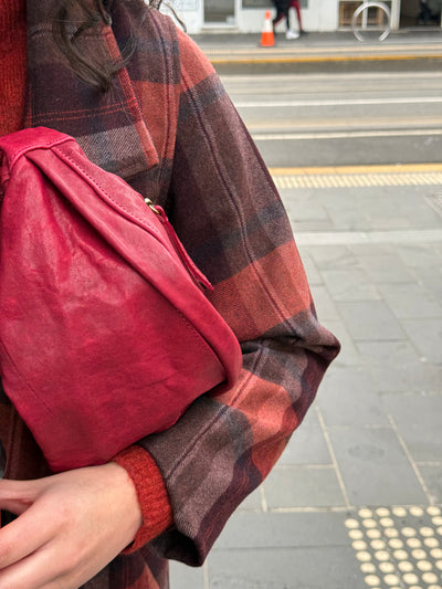 Person wearing a red and black plaid coat holding a red bag on a city street.