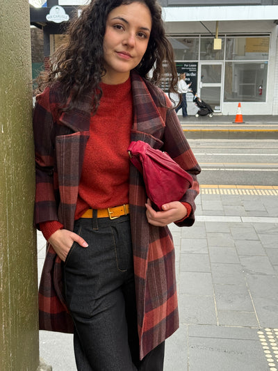 Woman in a red sweater and plaid coat standing on a city street.