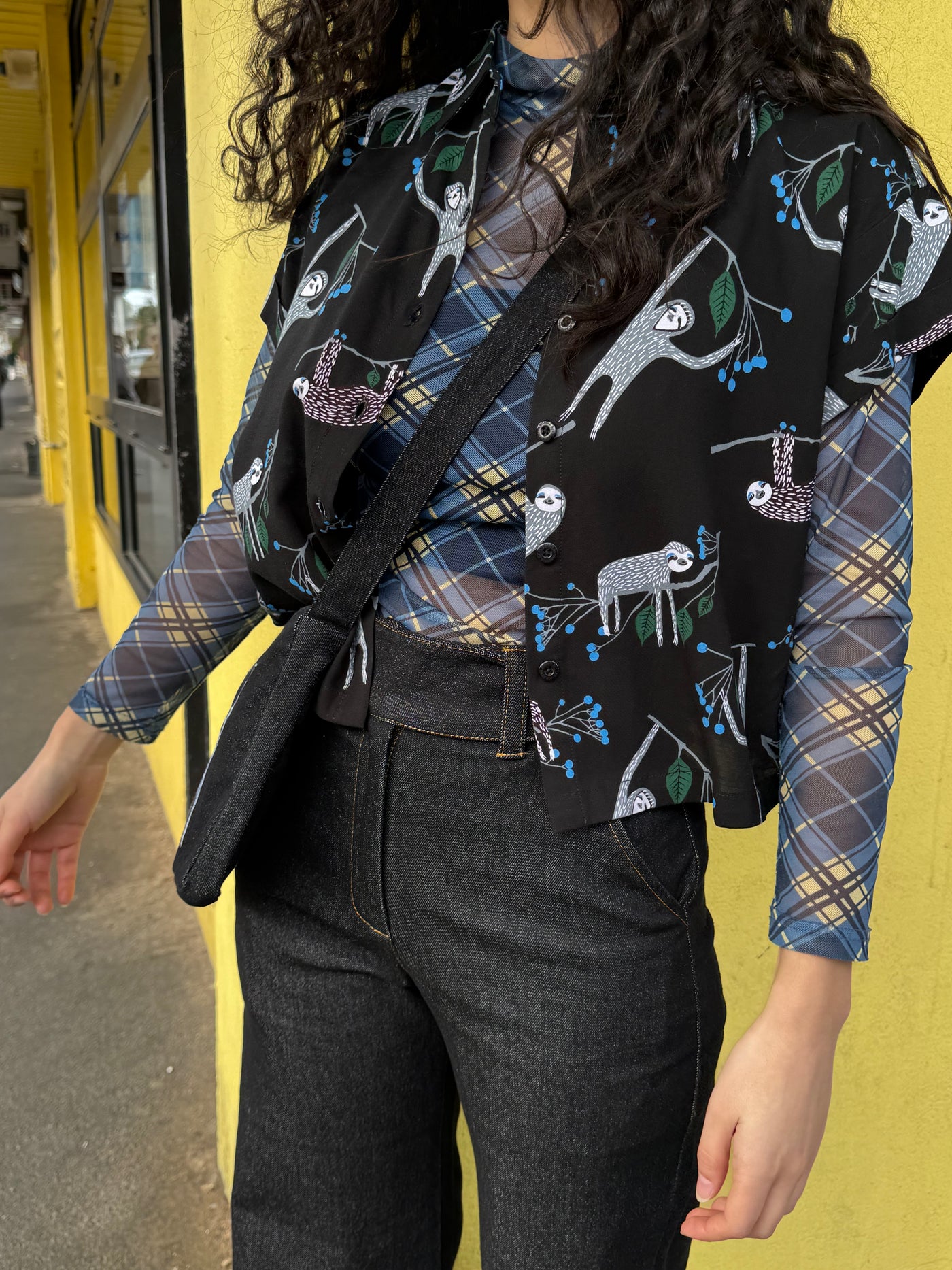 Person wearing a patterned shirt with plaid sleeves against a yellow wall.