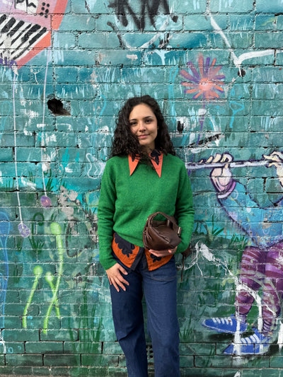 Person wearing a green sweater with orange accents in front of a colorful graffiti wall.