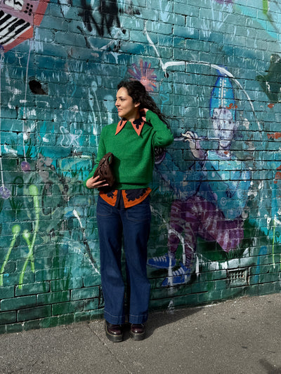 Woman in a green sweater and blue jeans standing against a graffiti-covered wall.
