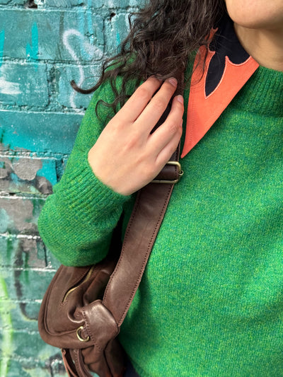 Person wearing a green sweater with a brown leather bag against a graffiti-covered wall.