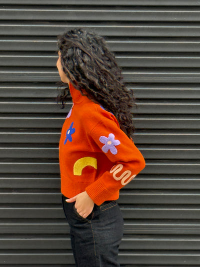 Person wearing an orange sweater with colorful designs against a gray background