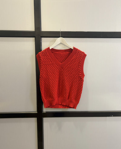 Red knitted vest on a hanger against a neutral background