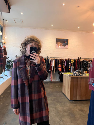 Person wearing a plaid coat in a store setting with shelves and products.