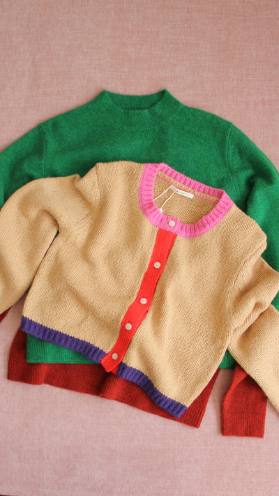 Stack of colorful sweaters on a pink background