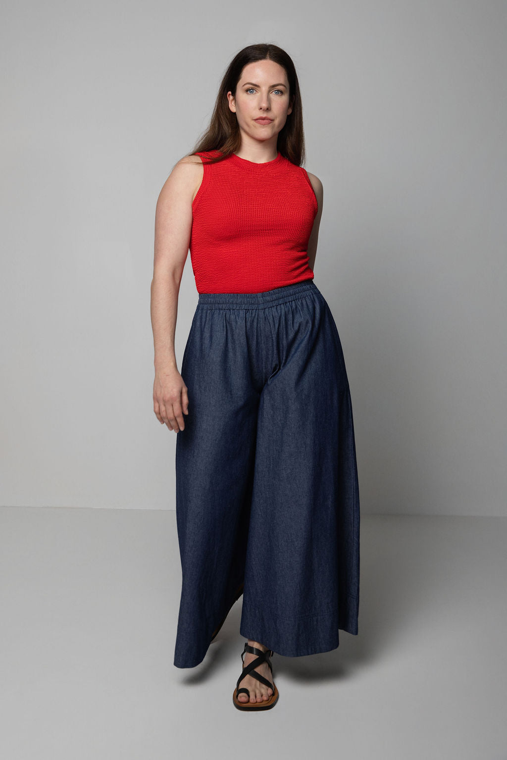 Woman wearing a red sleeveless top and blue wide-leg pants on a gray background
