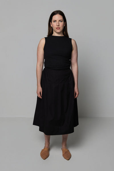 Woman wearing a black sleeveless top and black skirt against a plain background