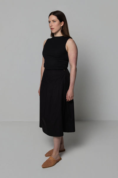 Woman wearing a black sleeveless top and skirt against a plain background