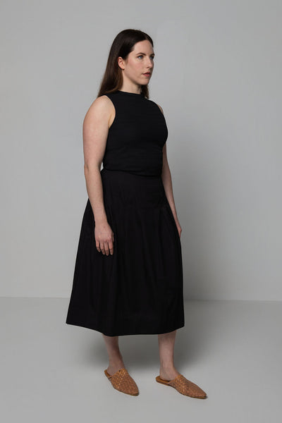 Woman wearing a black sleeveless top and skirt against a plain background