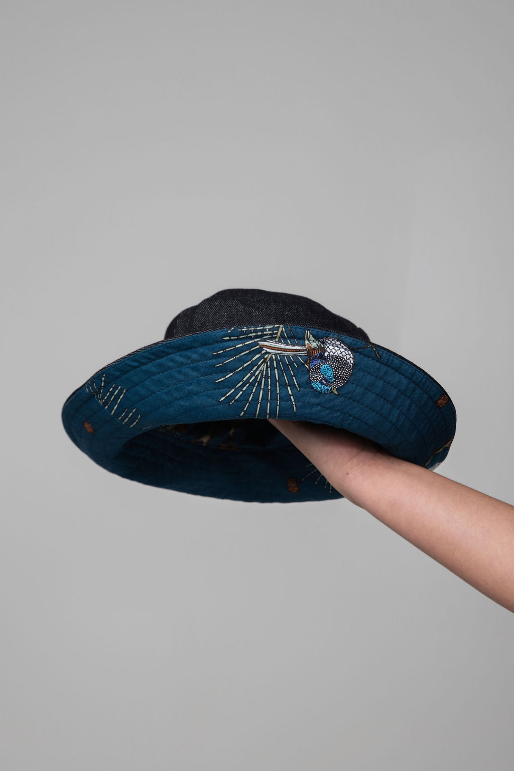 Navy blue bucket hat with bird print held by a hand against a gray background